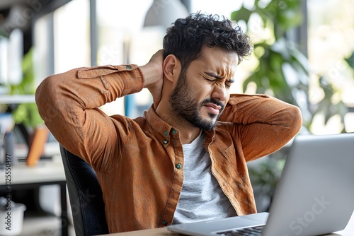 A man experiencing neck pain while working on laptop at desk