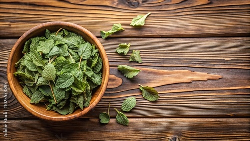 Dried lemon balm tea leaves in bowl on wooden table from above with copy space