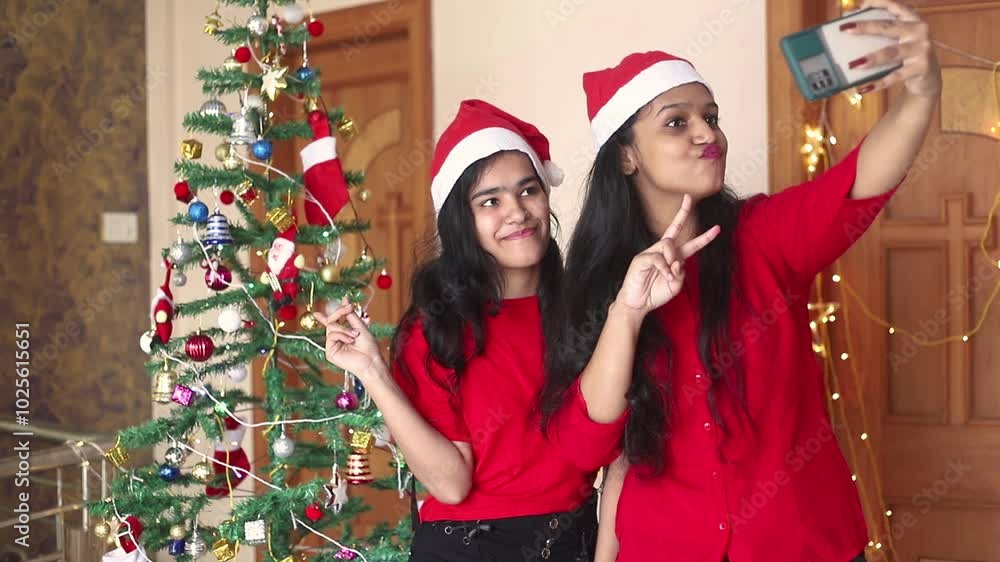 Young indian Gen Z girls friends wear santa hats celebrating christmas taking selfie picture with smart phone, Festive holidays, Xmas, Friendship, Technology. Young indian Gen Z girls friends wear santa hats celebrating christmas taking selfie picture with smart phone, Festive holidays, Xmas, Friendship, Technology.