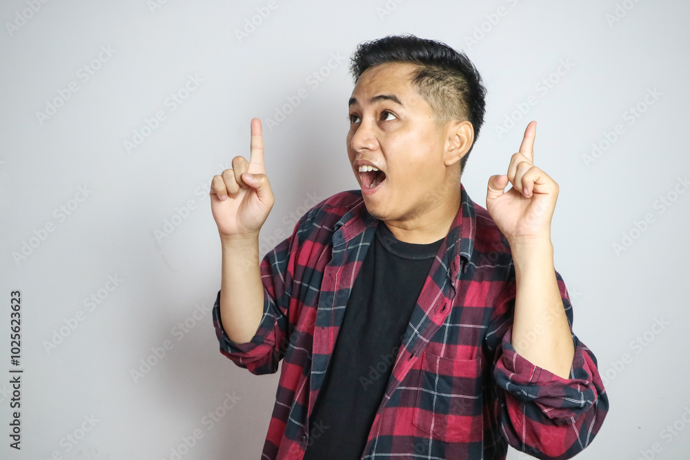 A young Asian man looks thoughtfully upward while pointing with his right index finger. The plain white background highlights the subject's contemplative A young Asian man looks thoughtfully upward while pointing with his right index finger. The plain white background highlights the subject's contemplative