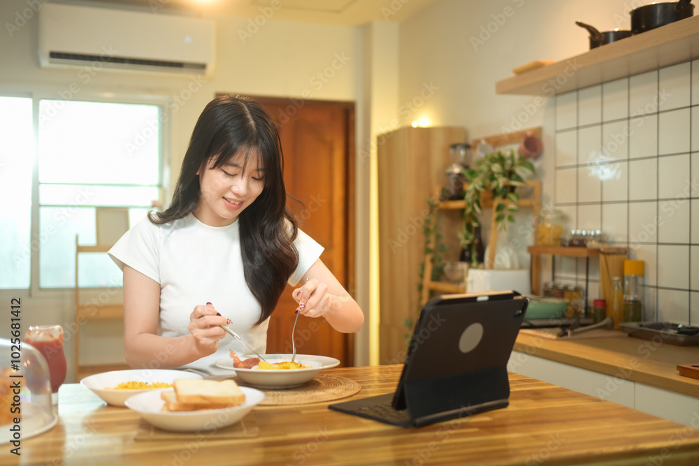 Attractive young woman enjoying her breakfast and using digital tablet at a kitchen table Attractive young woman enjoying her breakfast and using digital tablet at a kitchen table