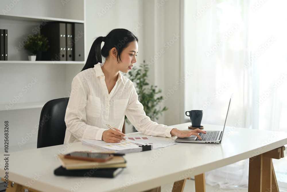 Focused young businesswoman working at a desk with laptop and document in a office Focused young businesswoman working at a desk with laptop and document in a office