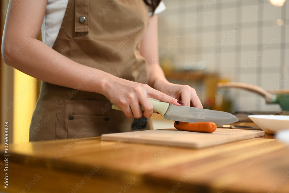 Close up of a woman cutting a sausage on wooden cutting board preparing ingredients for a meal Close up of a woman cutting a sausage on wooden cutting board preparing ingredients for a meal