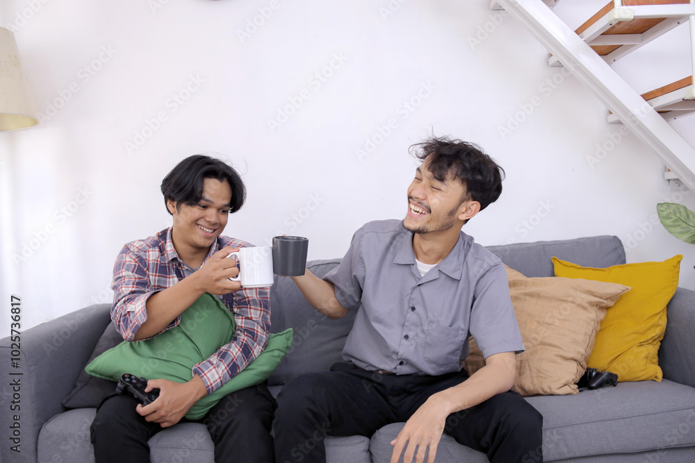 Two friends in casual wear talking and sitting on a couch in the living room while drinks coffee together Two friends in casual wear talking and sitting on a couch in the living room while drinks coffee together