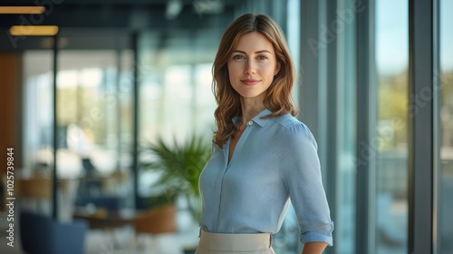 Confident woman in a modern office, smiling while standing near large windows with a view of greenery outside. Free Download Confident woman in a modern office, smiling while standing near large windows with a view of greenery outside. - GFXLoad