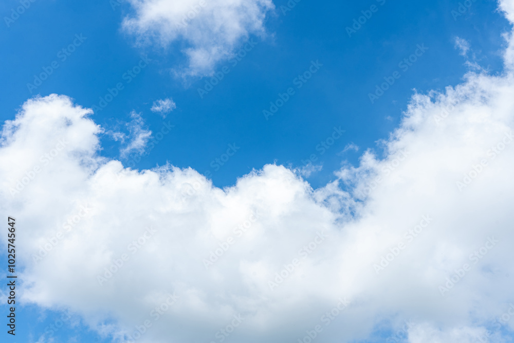 Fluffy white clouds drift across a clear blue sky, casting soft shadows on the landscape below Fluffy white clouds drift across a clear blue sky, casting soft shadows on the landscape below