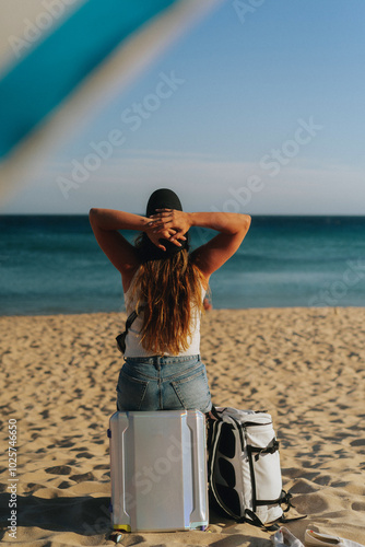A woman travels, sits on a suitcase on the beach.
