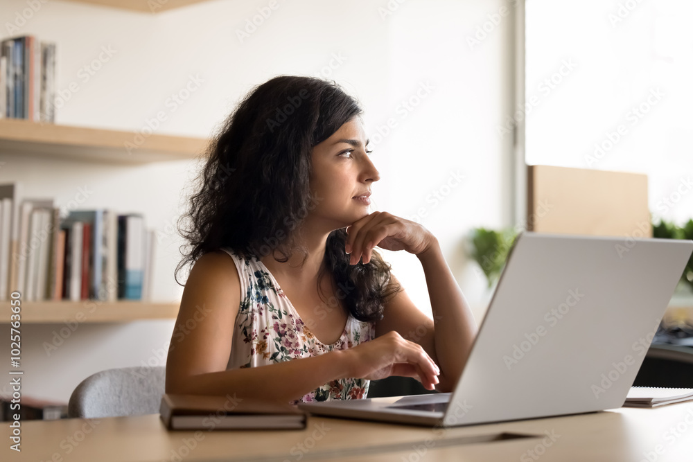 Serious pensive young Indian professional woman sitting at laptop at workplace, thinking on project decision, planning work strategy, touching chin in deep thoughts, looking at window, typing, Serious pensive young Indian professional woman sitting at laptop at workplace, thinking on project decision, planning work strategy, touching chin in deep thoughts, looking at window, typing,