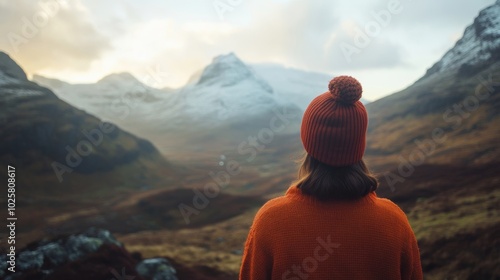 A person in a bright orange sweater and red hat admires stunning mountain scenery at sunset. Nature captivates with its beauty.