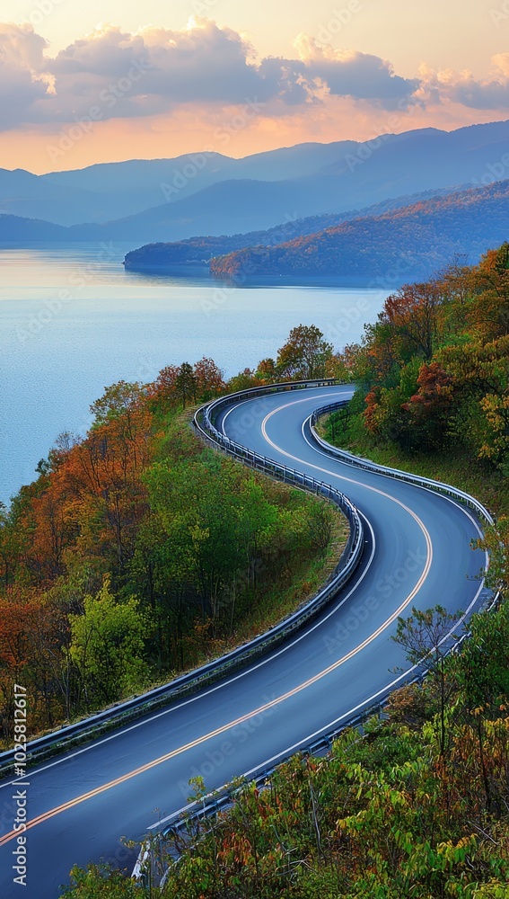 Obraz premium A curved road winds through the heart of a mountain range, leading the eye to a tranquil lake nestled in the distance Mountains rise majestically in the backdrop