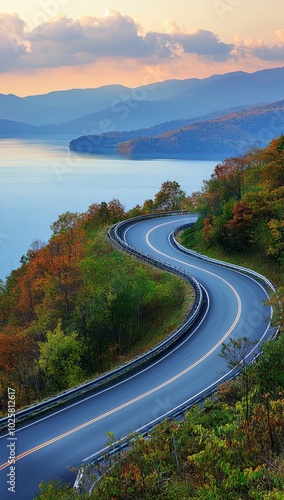  A curved road winds through the heart of a mountain range, leading the eye to a tranquil lake nestled in the distance Mountains rise majestically in the backdrop