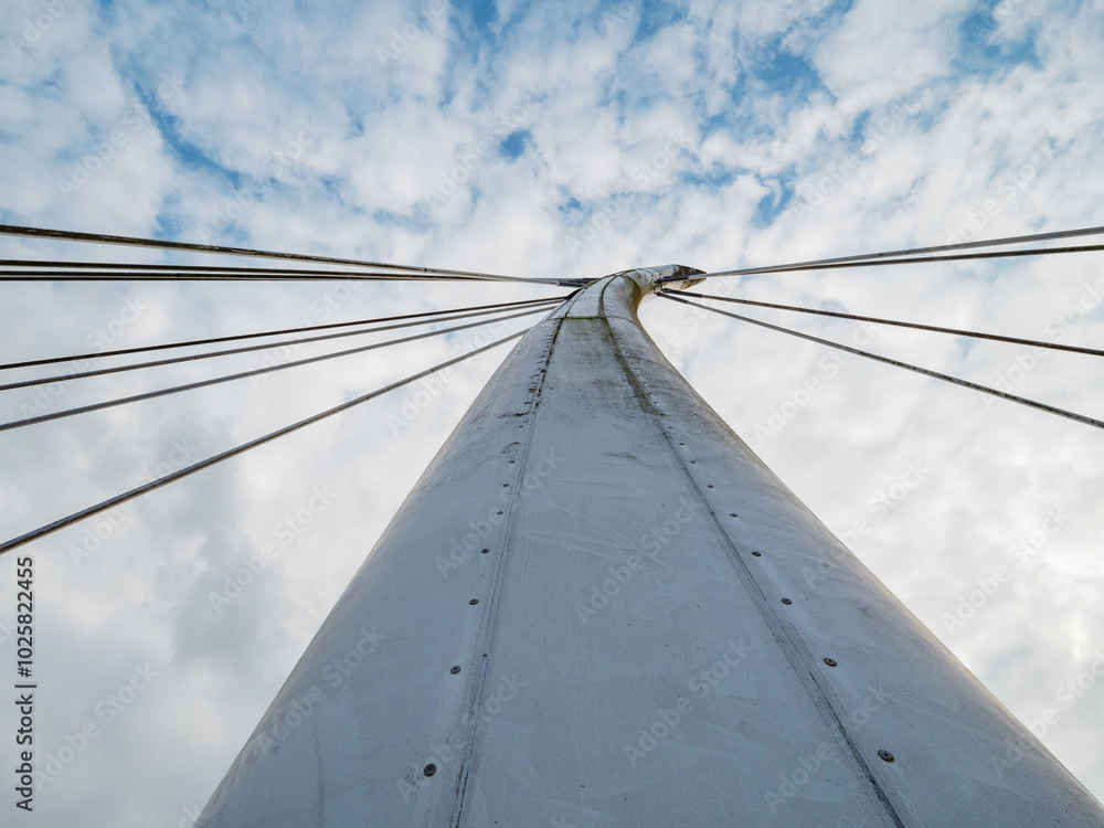 Fototapeta premium A bridge with a long white pillar and a cloudy sky in the background. The bridge is tall and the sky is overcast. Design and engineering. Modern bridge with suspension metal cords.