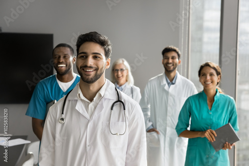 Happy motivated young male doctor posing in front of friendly diverse colleagues group. Millennial intern medic starting career at international clinic satisfied with professional growth opportunities photo