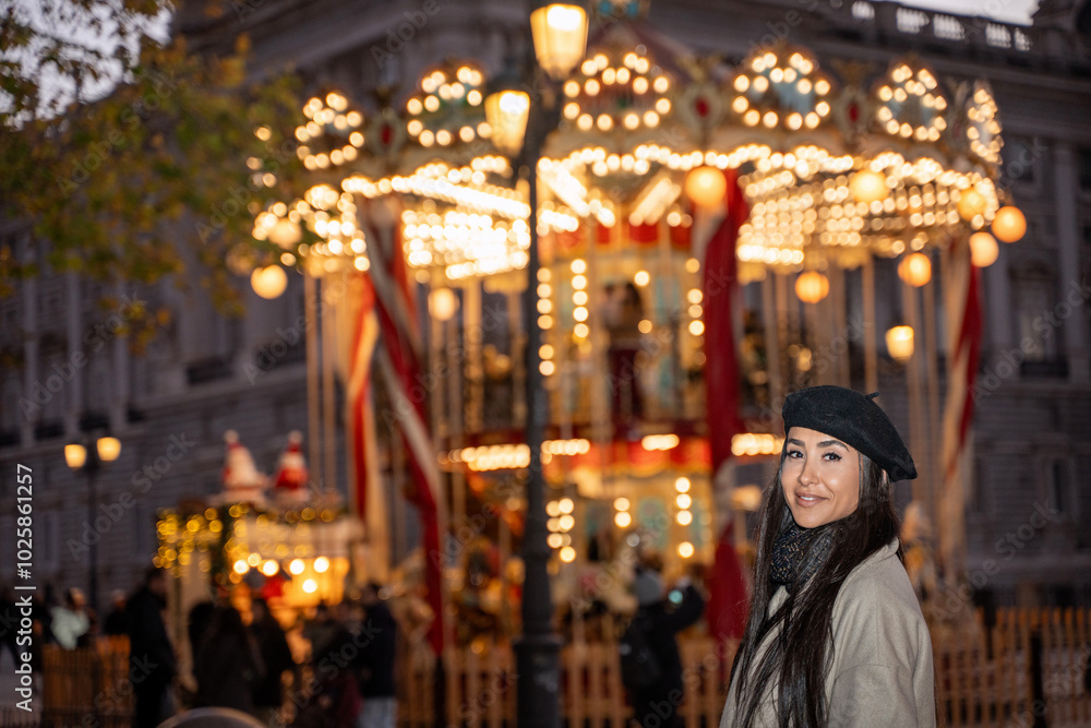 Young woman is posing in front of a carousel at a christmas market, wearing a beige coat and a black beret Young woman is posing in front of a carousel at a christmas market, wearing a beige coat and a black beret