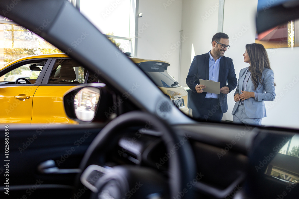 Car dealership manager helps a client choose a car. sales manager selling electric car to a female customer at showroom. Beautiful Caucasian female client customer choosing new car. Car dealership manager helps a client choose a car. sales manager selling electric car to a female customer at showroom. Beautiful Caucasian female client customer choosing new car.