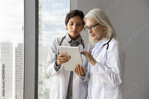 Bild auf Leinwand Young female doctor intern meet older age colleague ask question about patient history case show labs radiology results on tablet screen