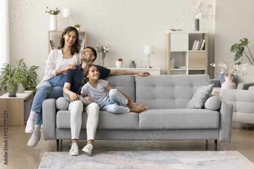 Happy homeowners. Friendly family married couple preteen age daughter spend time together cuddling on couch at cozy living room talk laugh enjoy being renters tenants of modern apartment. Copy space
