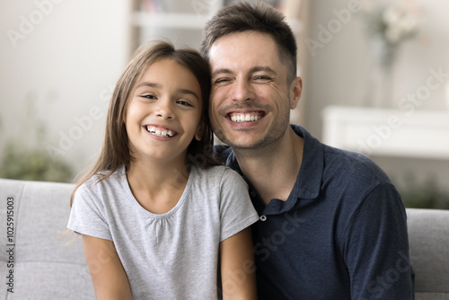 Happy single parenting. Head shot portrait young man father grown up elder brother babysitter little tween age girl daughter younger sister ward cuddle on sofa look at camera with happy white smiles photo