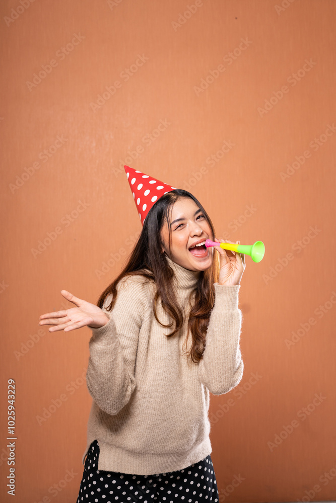 A joyful woman in a colorful party hat celebrates at a fun gathering with a whistle A joyful woman in a colorful party hat celebrates at a fun gathering with a whistle