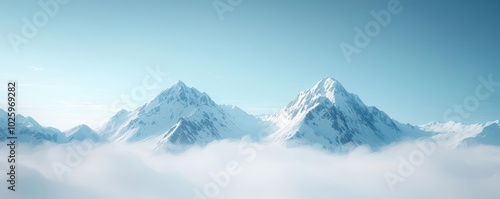 Snow-covered mountains peering above a serene, misty landscape under a clear blue sky.