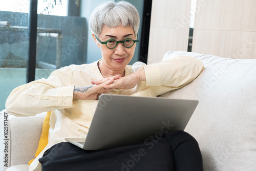 A woman in glasses is sitting on a couch and using a laptop. She is focused on her work or browsing the internet. Concept of productivity and relaxation