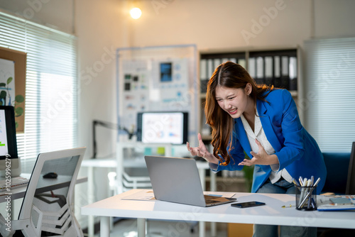 A woman in a blue jacket is sitting at a desk with a laptop in front of her