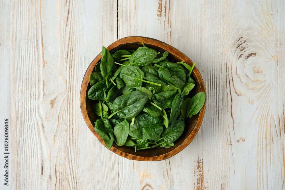 Freshly harvested spinach leaves in a wooden bowl on a rustic wooden table Freshly harvested spinach leaves in a wooden bowl on a rustic wooden table