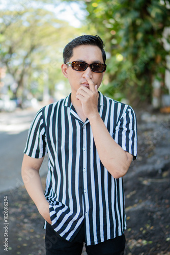 A fashionable young man poses confidently wearing sunglasses and a striped shirt.