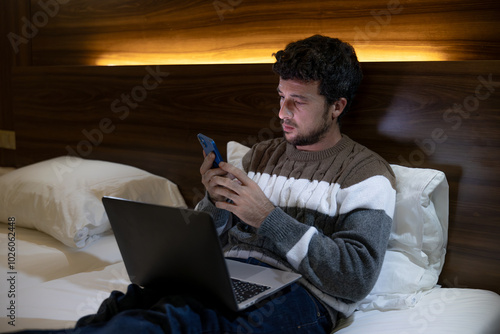 Happy young entrepreneur man on business trip works in the hotel room with his laptop and phone or smartphone