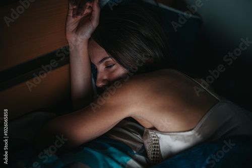 A woman sleeps peacefully on a bed, conveying tranquility and restfulness. The dim lighting and cozy surroundings enhance the serene ambiance, capturing a quiet moment of relaxation. photo