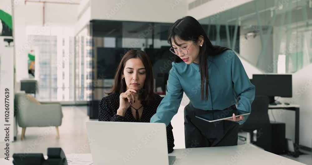 Two multi-ethnic women colleagues working together in office, engaged in collaborative discussion, reviewing and analyzing important documents or data displayed on laptop. Teamwork and productivity Two multi-ethnic women colleagues working together in office, engaged in collaborative discussion, reviewing and analyzing important documents or data displayed on laptop. Teamwork and productivity