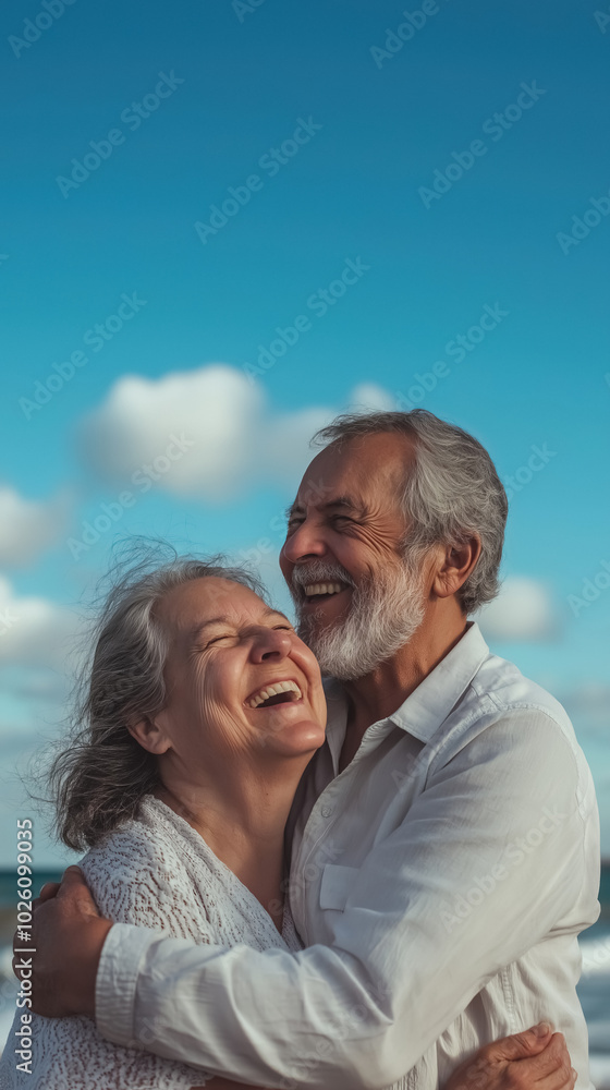 A happy elderly couple embracing and laughing on the shore, with the ocean stretching behind them and the blue sky overhead A happy elderly couple embracing and laughing on the shore, with the ocean stretching behind them and the blue sky overhead