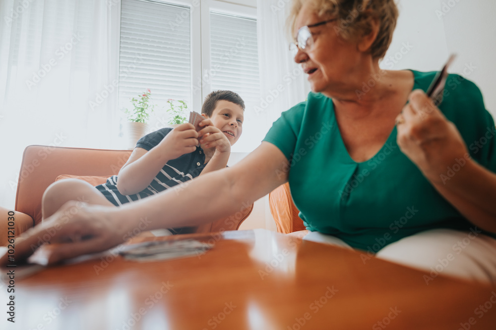 A joyful moment shared between a grandmother and her grandson as they play cards at home, highlighting family bonding and fun. A joyful moment shared between a grandmother and her grandson as they play cards at home, highlighting family bonding and fun.