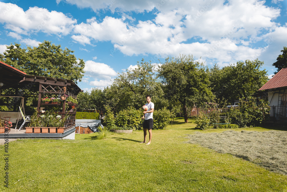 player practices a volleyball bump in a garden full of trees and grass. He is dressed in a white t-shirt and black shorts, barefoot. The blue sky with white clouds enhances the summer atmosphere player practices a volleyball bump in a garden full of trees and grass. He is dressed in a white t-shirt and black shorts, barefoot. The blue sky with white clouds enhances the summer atmosphere