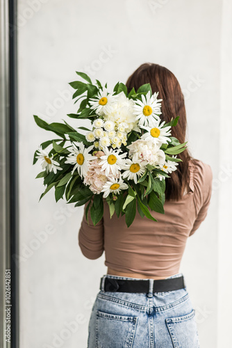 The girl stands back and holds a bouquet of daisies in her hands