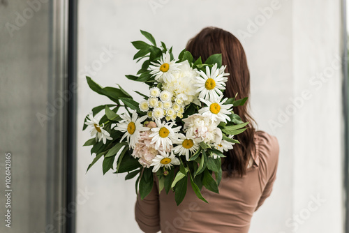 The girl stands back and holds a bouquet of daisies in her hands