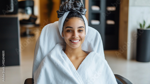 A smiling young woman wrapped in a plush towel, her hair freshly washed and ready for treatment, sitting in a modern, minimalist salon, embodying the luxury of self-care and wellne photo