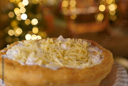 Close up of a langos, typical Hungarian food specialty, with sour cream and cheese on a white dish in hand, deep fried doughin front of christmas lights at a christmas market