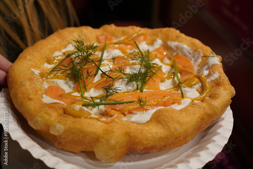 Close up of a langos, typical Hungarian food specialty, with sour cream and fish salmon on a white dish on a brown table, deep fried dough at a christmas market
