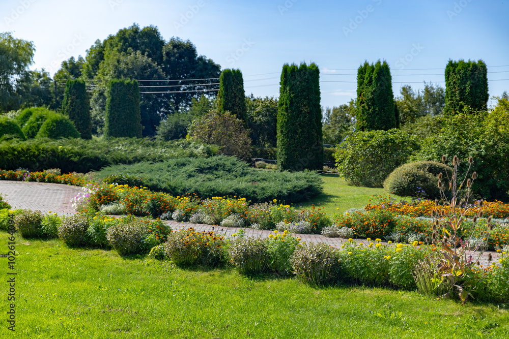 A stone path winds through a lush green grassy area, leading towards a small wooden bridge. On the other side of the path, a pond filled with lily pads and reeds adds a touch of natural beauty. A stone path winds through a lush green grassy area, leading towards a small wooden bridge. On the other side of the path, a pond filled with lily pads and reeds adds a touch of natural beauty.