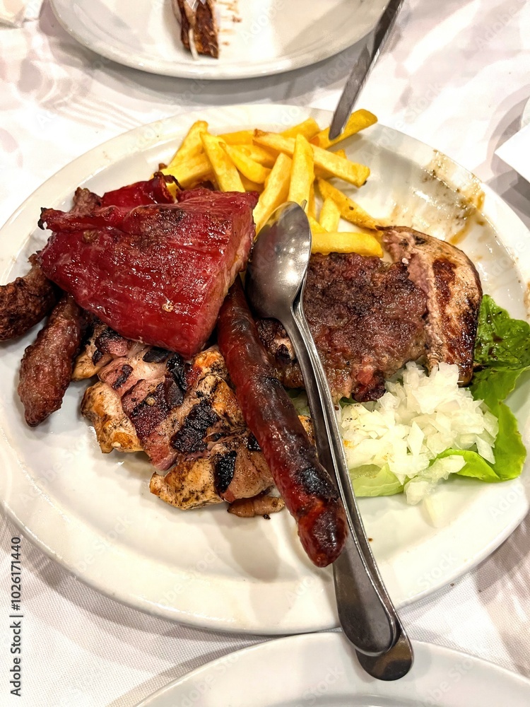 Sausage and several types of grilled meat served on a plate with French fries and salad