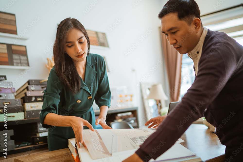 Fototapeta premium beautiful shopkeeper showing the male customer the catalogue book of the window treatments