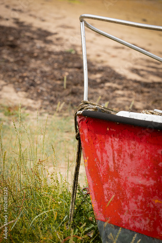 The bow of a red-hulled boat. A boat sits on the sand, close-up on the bow.