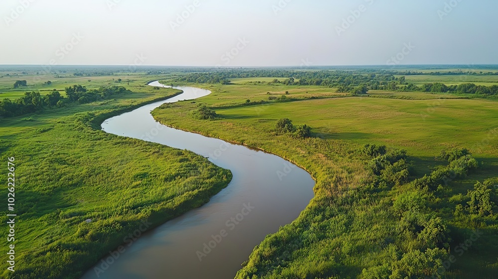 Obraz premium Drone view of a winding river flowing through lush green farmland. 