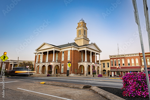 Fototapeta Naklejka Na Ścianę i Meble -  Morning traffic headlights illuminate the downtown square in Lancaster, Kentucky, with the historic courthouse as a backdrop in this small American town.
