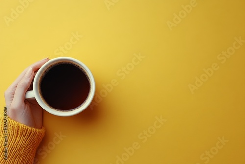 A hand holding a steaming cup of coffee against a bright yellow background in...