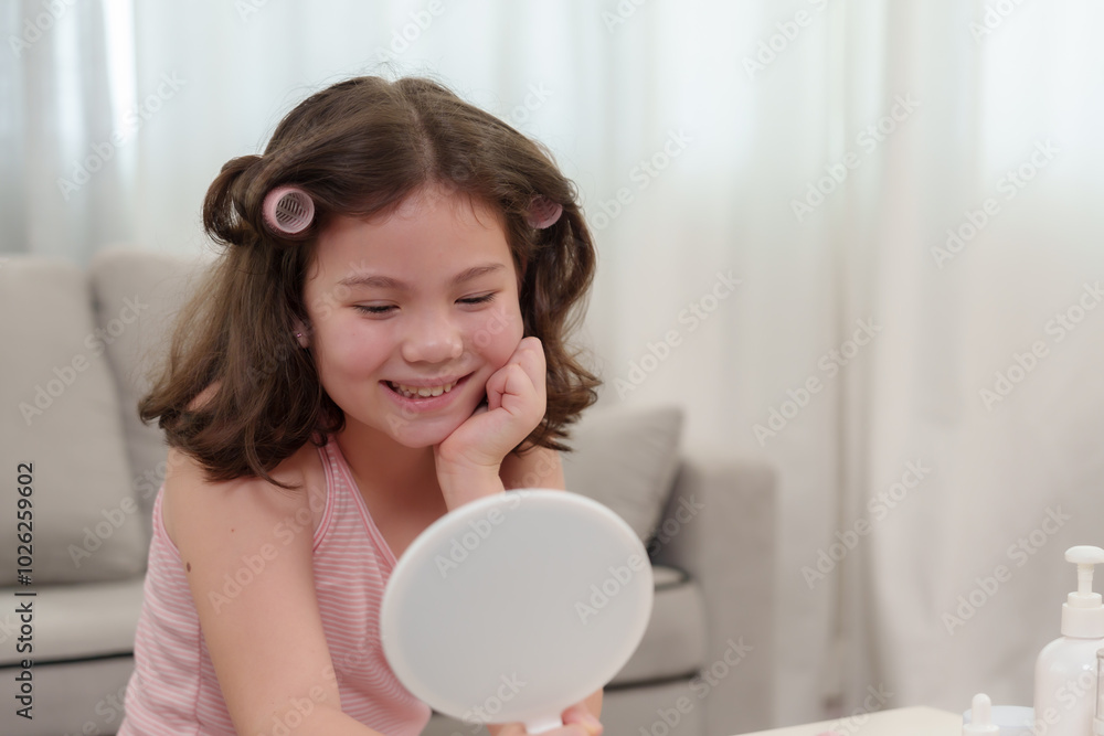 Smiling young girl looking at mirror while preparing hair with pink curlers. Scene captures playful, cheerful moment in cozy home setting. Warm, natural light fills room creating relaxed mood. Smiling young girl looking at mirror while preparing hair with pink curlers. Scene captures playful, cheerful moment in cozy home setting. Warm, natural light fills room creating relaxed mood.