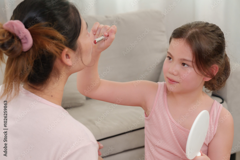 Young girl carefully applies lipstick to mother while holding mirror. Sweet moment captures love and playfulness between mother and daughter as they enjoy bonding through makeup activities. Young girl carefully applies lipstick to mother while holding mirror. Sweet moment captures love and playfulness between mother and daughter as they enjoy bonding through makeup activities.