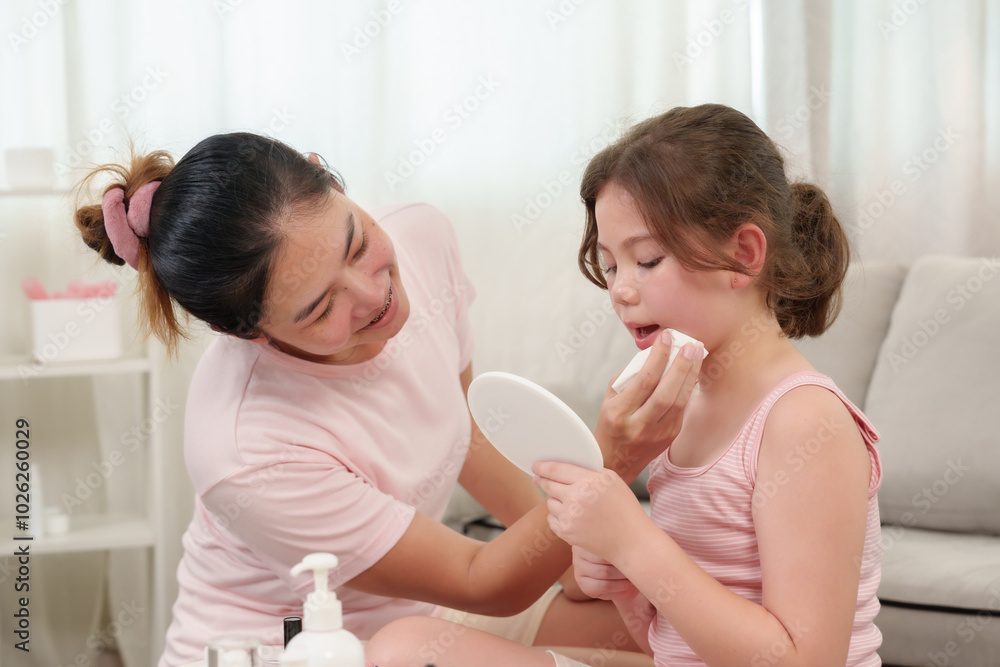 Mother lovingly helps daughter wipe makeup during a playful beauty session. Both share smiles, highlighting a heartwarming bonding moment as they enjoy a self-care routine together. Mother lovingly helps daughter wipe makeup during a playful beauty session. Both share smiles, highlighting a heartwarming bonding moment as they enjoy a self-care routine together.