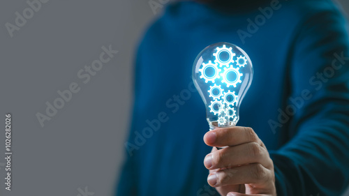 Person holding a light bulb with gear symbols inside, representing innovation, creativity, and new ideas in technology and business. photo